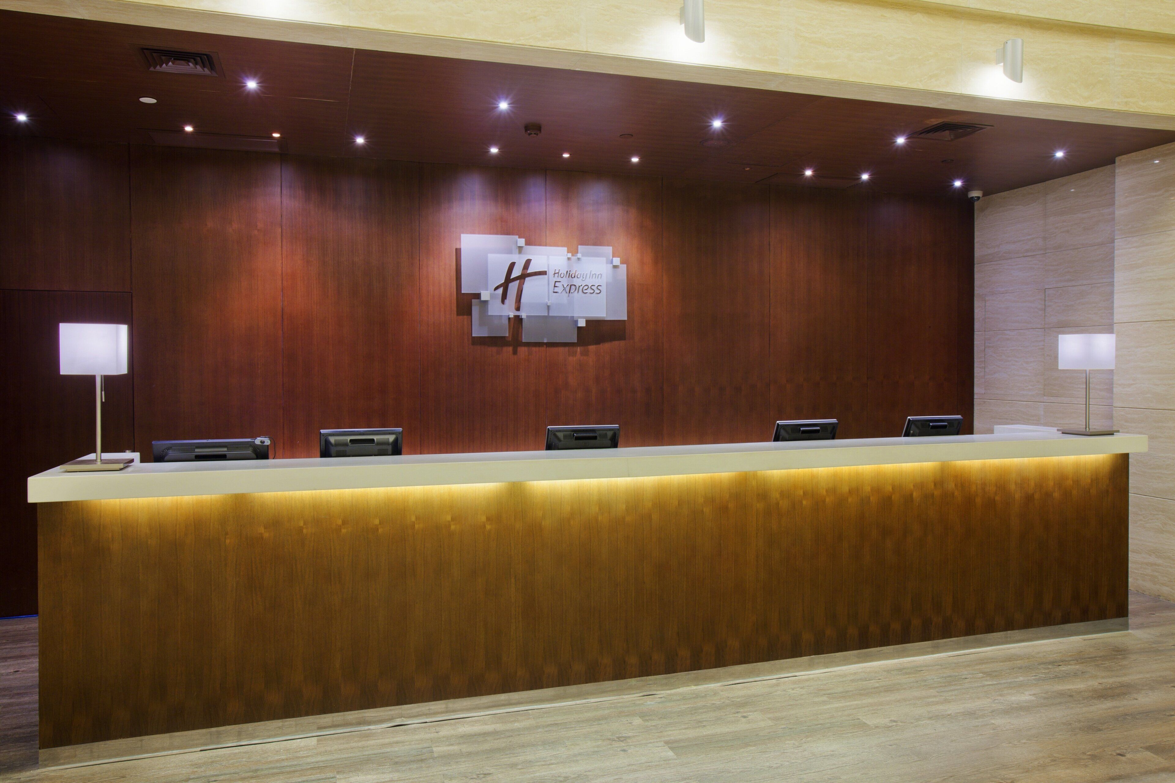 A reception desk with a wooden finish, a sign above it, and a series of lights on the ceiling.