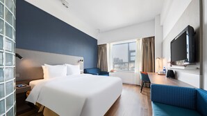 Et hotelværelse med en stor seng, et skrivebord, en blå sofa, et fjernsyn og et vindue med gardiner.