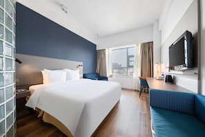 A hotel room with a large bed, a desk, a blue sofa, a TV, and a window with curtains. - Holiday Inn Express Suzhou Changjiang by IHG (Suzhou)