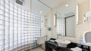 Et moderne badeværelse med en glasbrusekabine, et stort spejl og en bordplade i sort marmor.