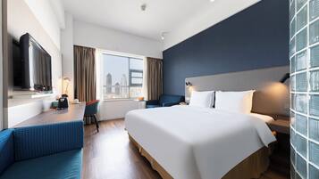 Habitación de hotel con cama, escritorio, silla, televisor y ventana con vista a la ciudad.