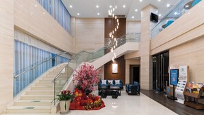 En moderne hotellobby med trappe, siddeområde og en digital informationsskærm.