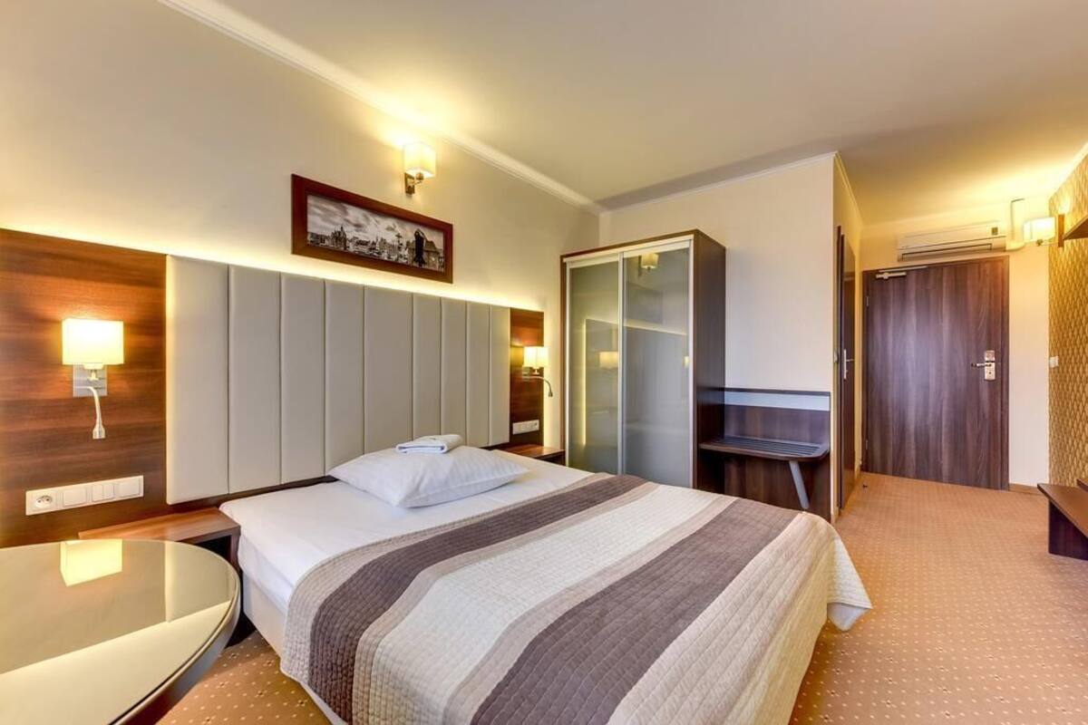 A hotel room with a bed, bedside table, lamp, wardrobe, and a mirror.