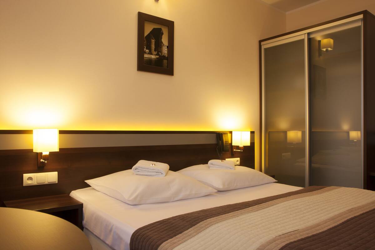 A hotel room with a bed, two bedside lamps, a nightstand, a framed picture on the wall, and a wardrobe.
