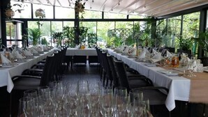 Une longue table à manger, dressée pour un événement formel, avec de nombreuses chaises, des nappes blanches et de la verrerie.