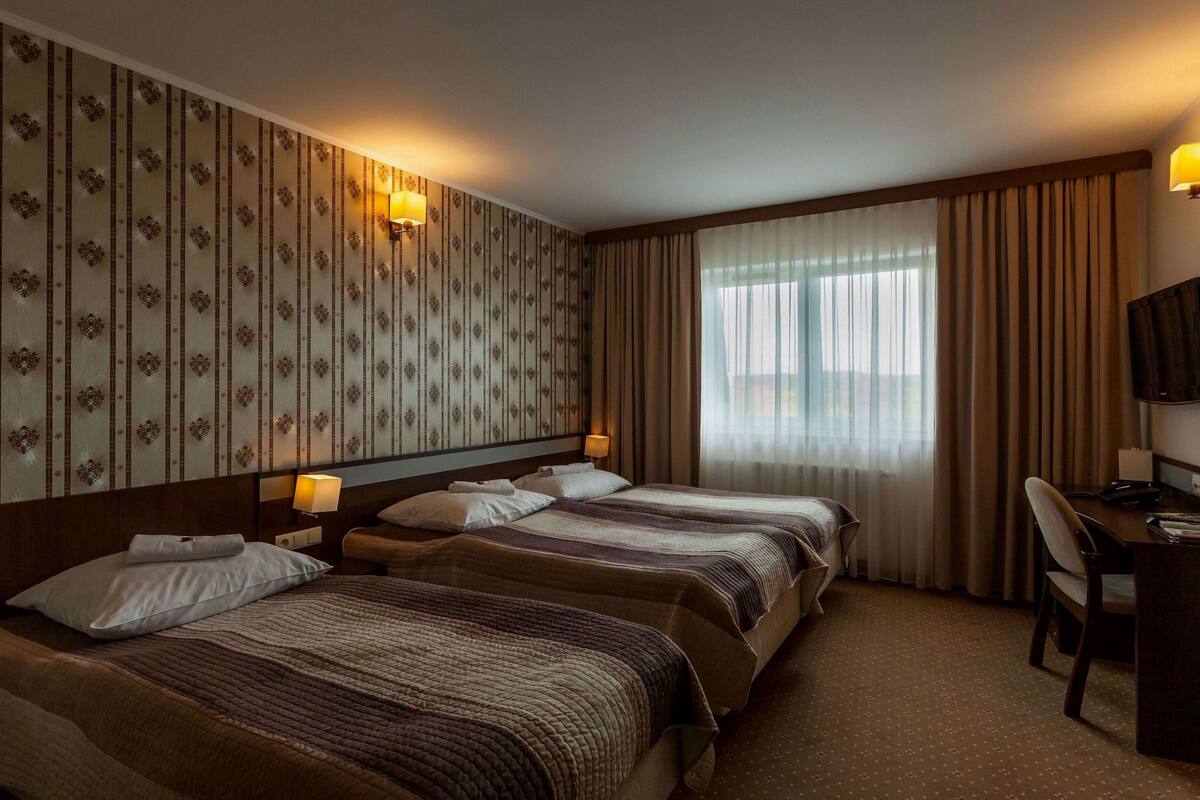 A hotel room with two beds, a desk, and a television.