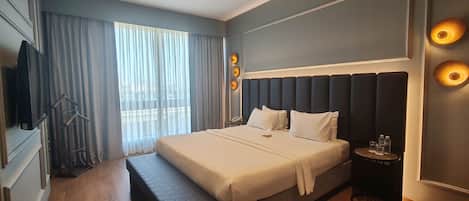 A modern hotel room with a large bed, a bedside table with a lamp, and a view of the city through the window.