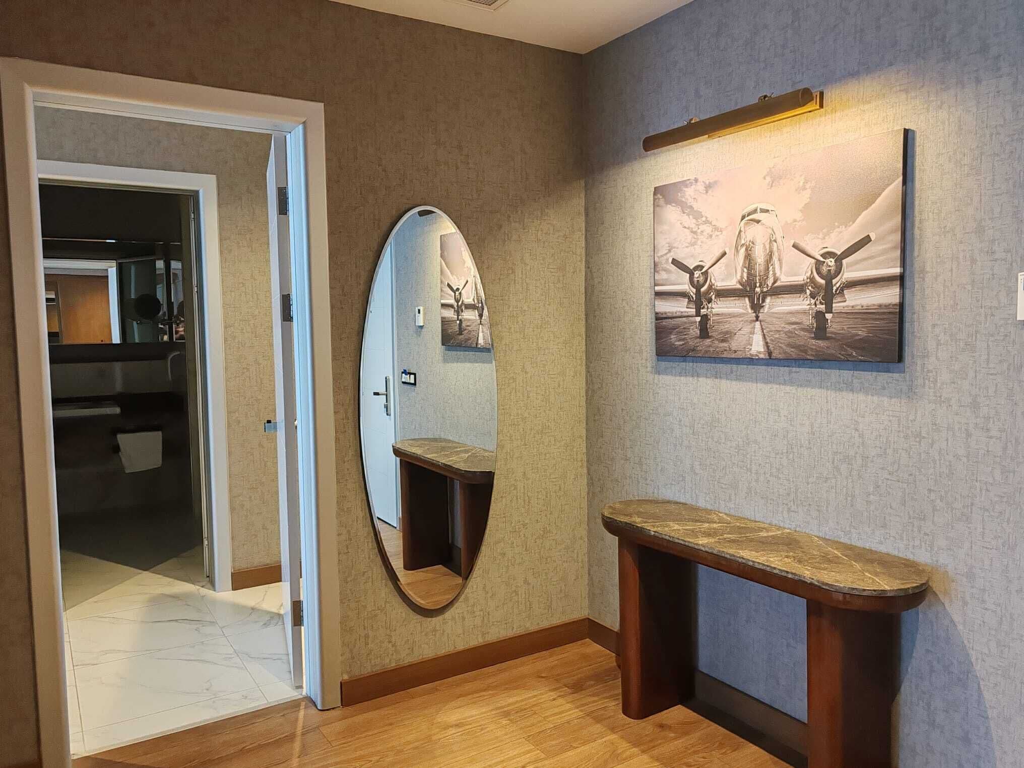 Un couloir d’hôtel avec un banc en bois, un grand miroir et un tableau encadré accroché au mur.