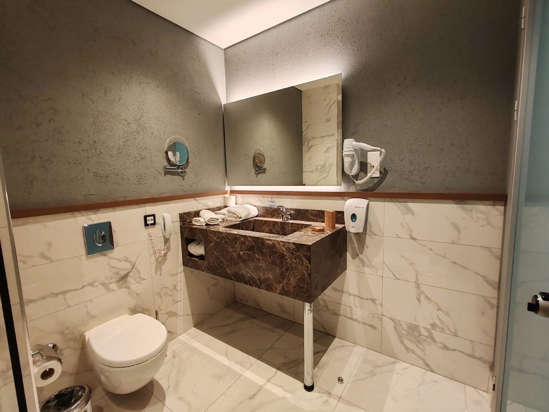 Une salle de bain avec un lavabo en marbre, des toilettes, un miroir et un sèche-cheveux.