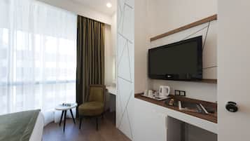 Habitación de hotel con una cama, una mesita con una silla, un televisor en la pared y una ventana con cortinas.