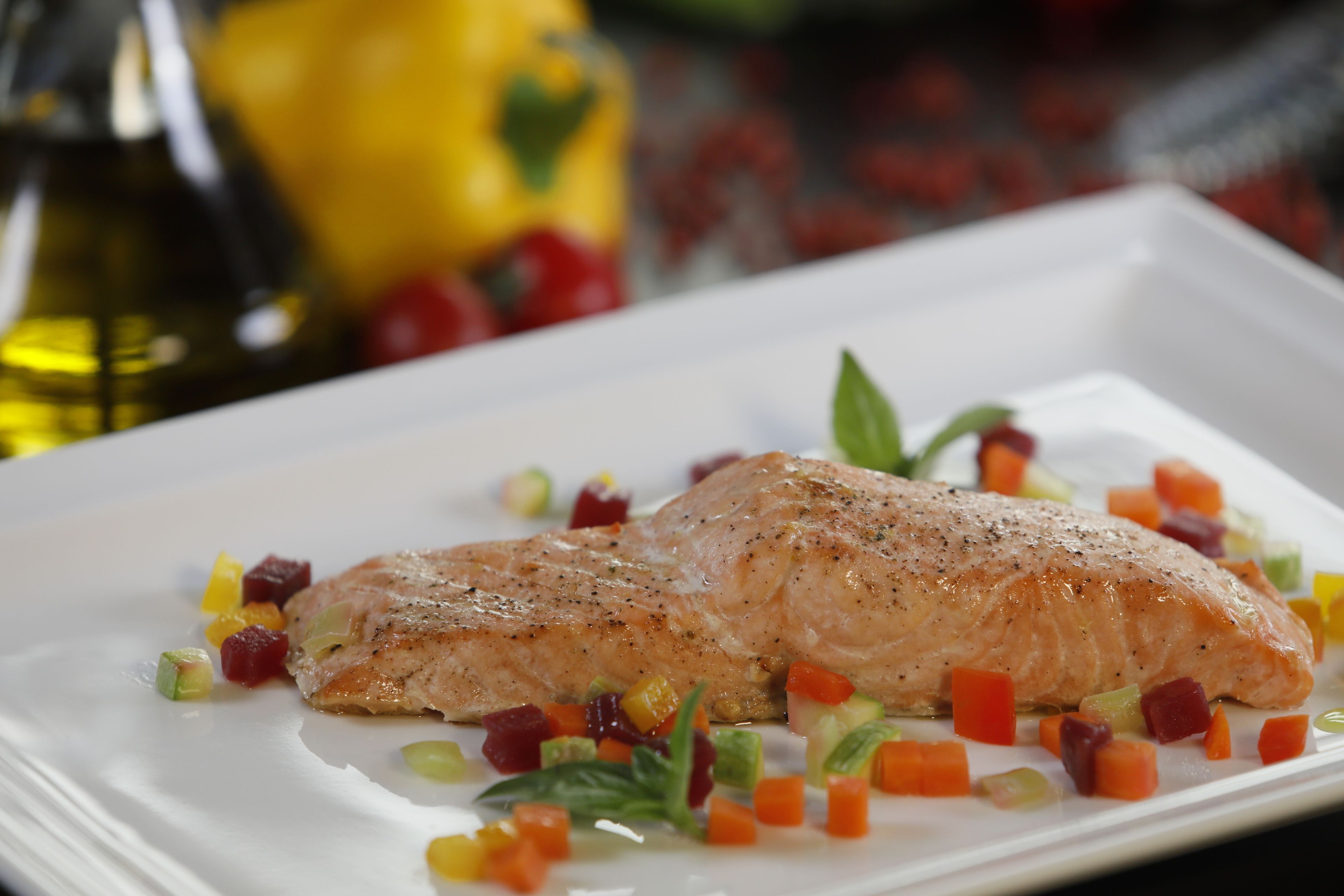 A white plate with a piece of salmon and diced vegetables.