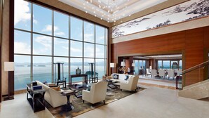 Un vestíbulo amplio con ventanas grandes que ofrecen vistas al mar, un candelabro y una escalera que conduce a un nivel superior.