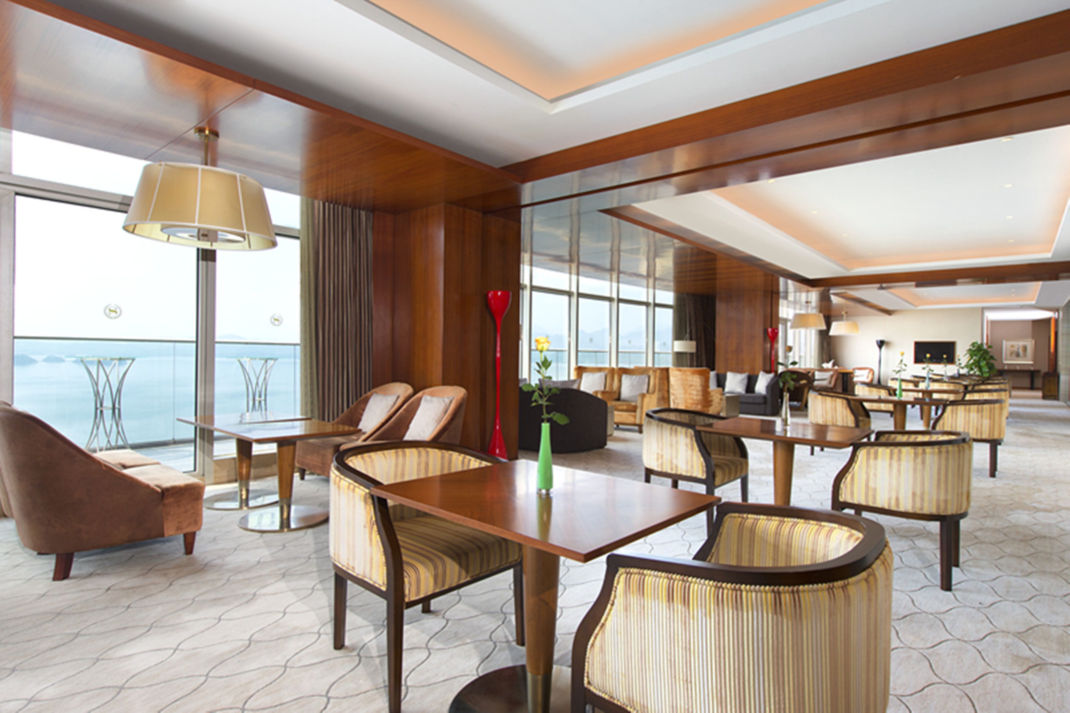A spacious hotel lobby with a large dining area, comfortable seating, and a view of the sea.