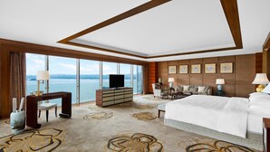 Habitación de hotel con una ventana grande, una cama, un escritorio, un televisor y vista al mar.