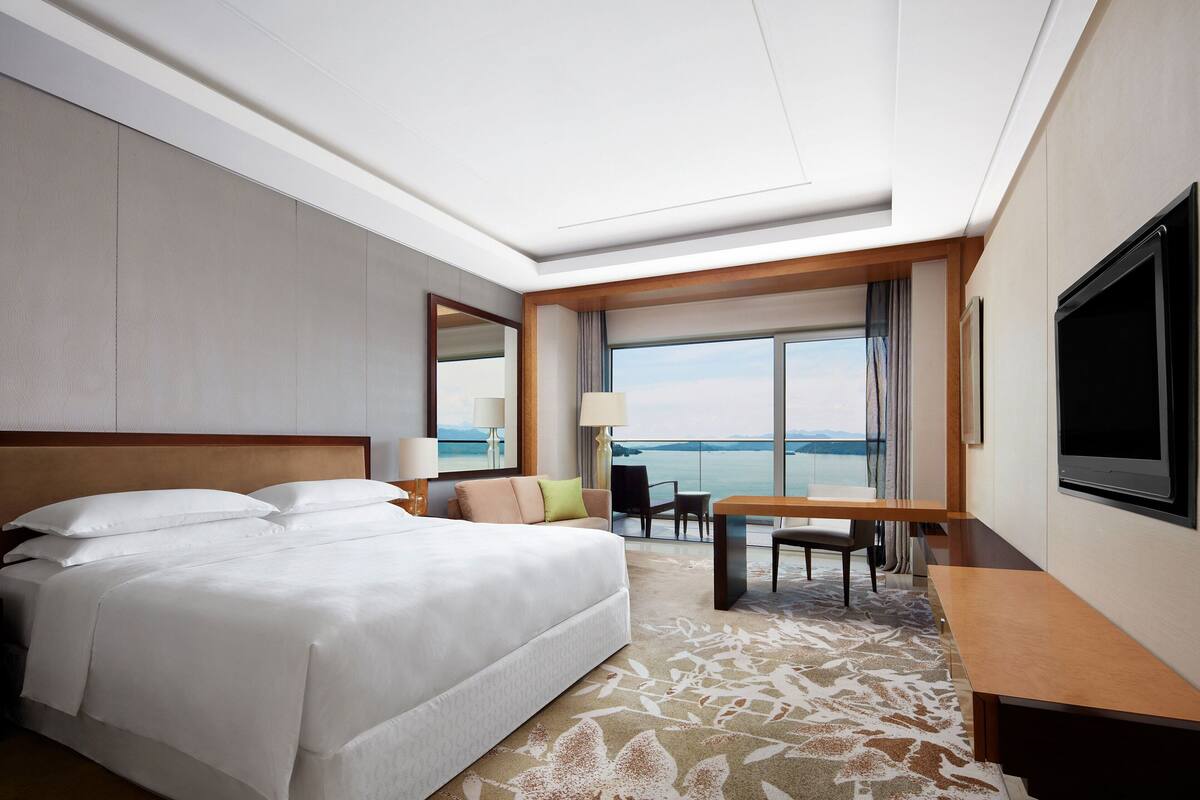 A hotel room with a large bed, a dining area, and a view of the sea.