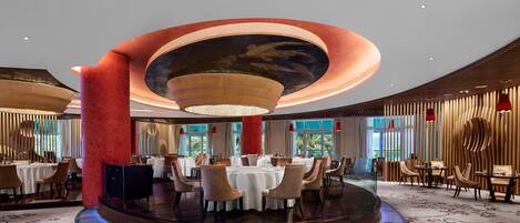 A modern dining area with round tables, red columns, and a central stage.
