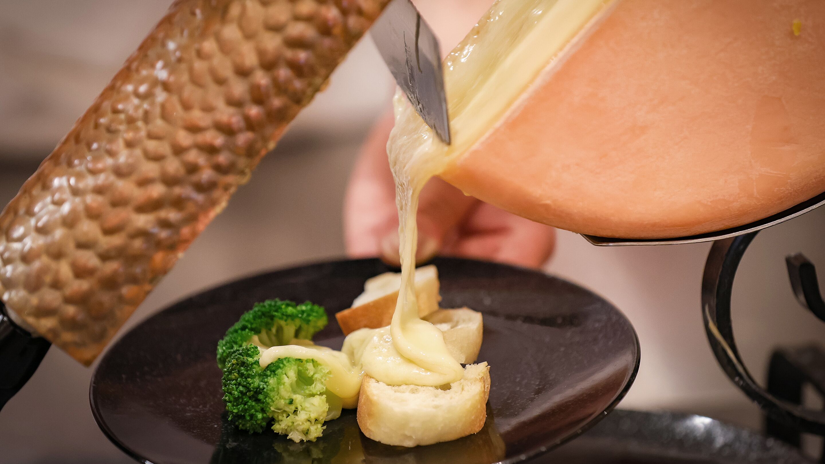 A person pouring a creamy substance over a dish with bread and broccoli.