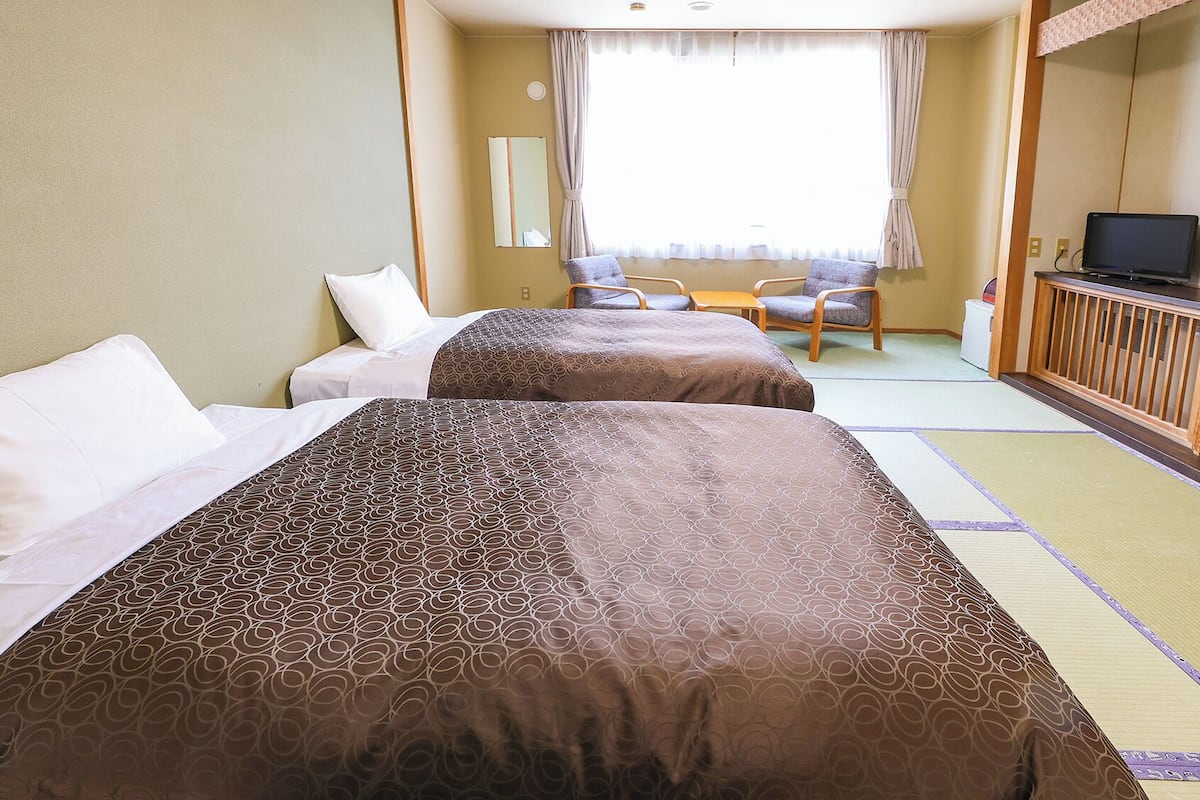 Une chambre d’hôtel avec deux lits, un bureau, une chaise, une télévision et une grande fenêtre avec des rideaux.