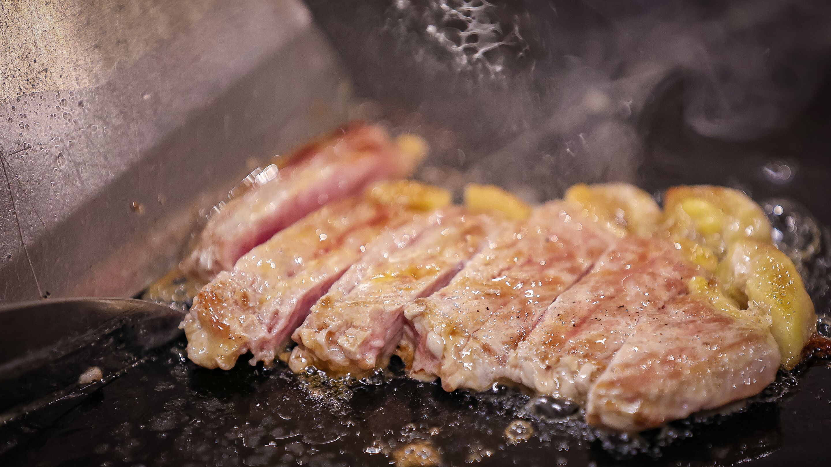 Primer plano de un bistec cocinándose en una parrilla, con marcas visibles de la parrilla y aceite.