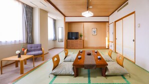 Una habitación tradicional japonesa con suelo de tatami, una mesa de madera baja, esteras de tatami, un sofá, un televisor y puertas correderas.