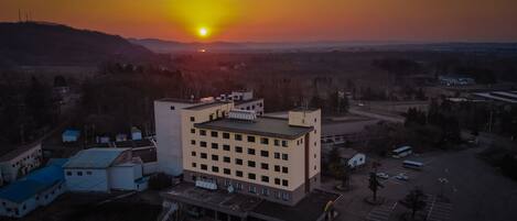 An aerial view of a building complex with multiple buildings, parking areas, and surrounding landscape during sunset.