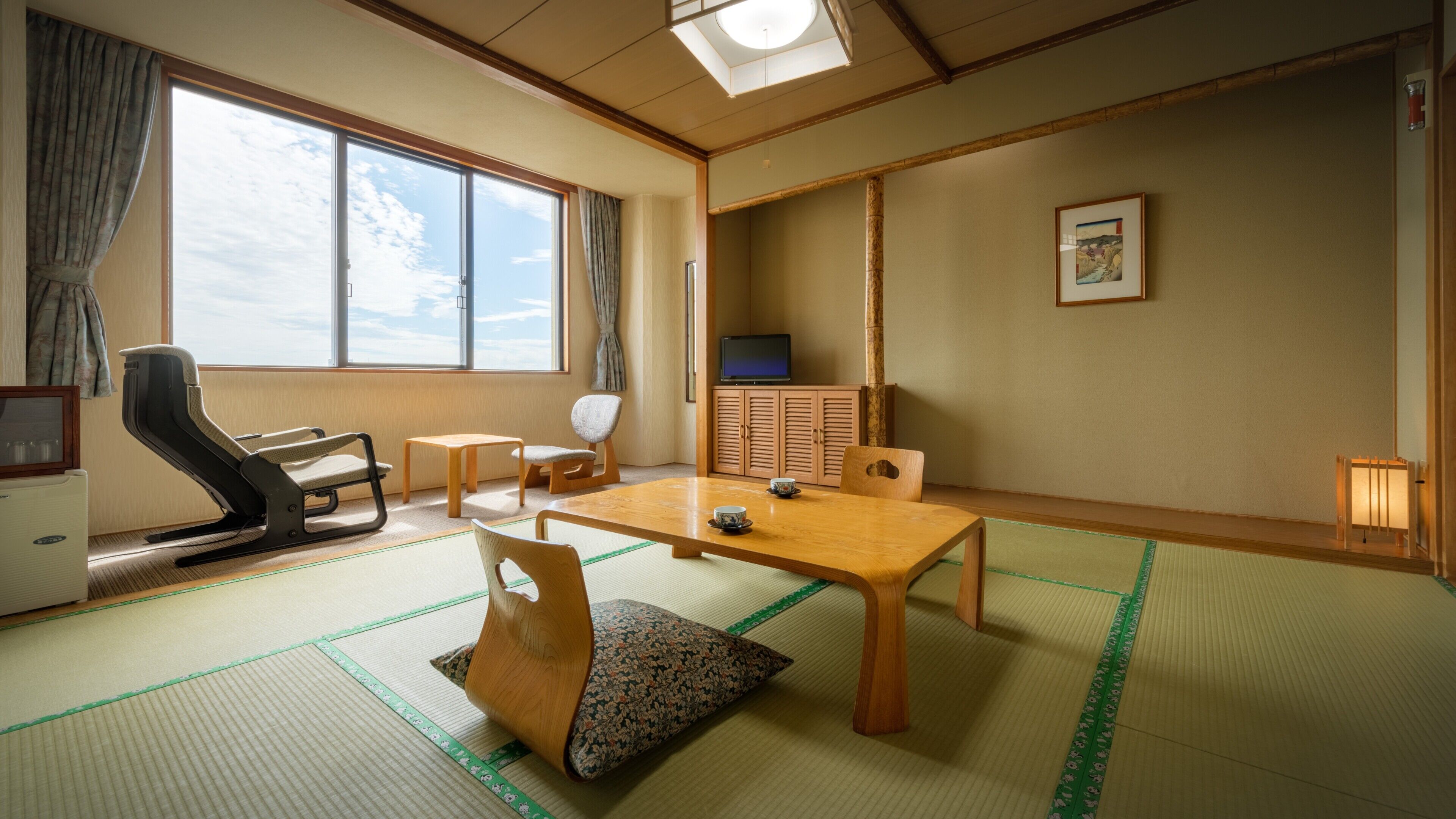 A traditional Japanese room with tatami flooring, a low table, chairs, a television, and a sliding door.