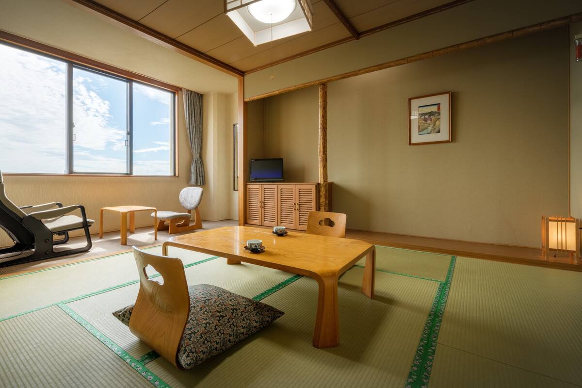 A traditional Japanese room with tatami flooring, a low table, chairs, a television, and a sliding door.