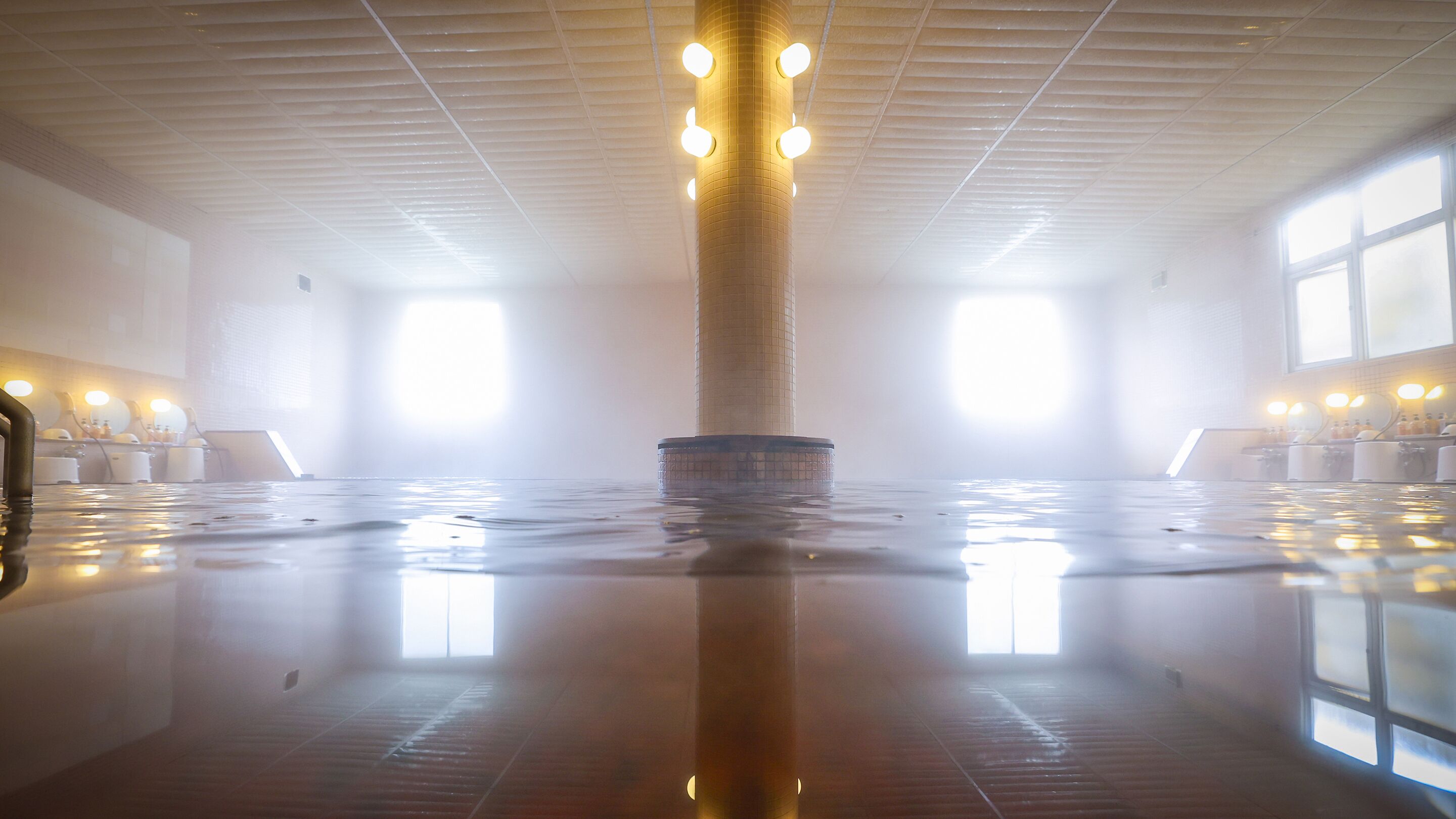 Un espacio interior amplio con una columna central, ventanas grandes y un suelo reflectante.