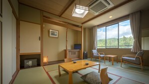 Una habitación tradicional japonesa con suelo de tatami, una mesa baja con cojines, un televisor y vistas a un bosque a través de un ventanal grande.