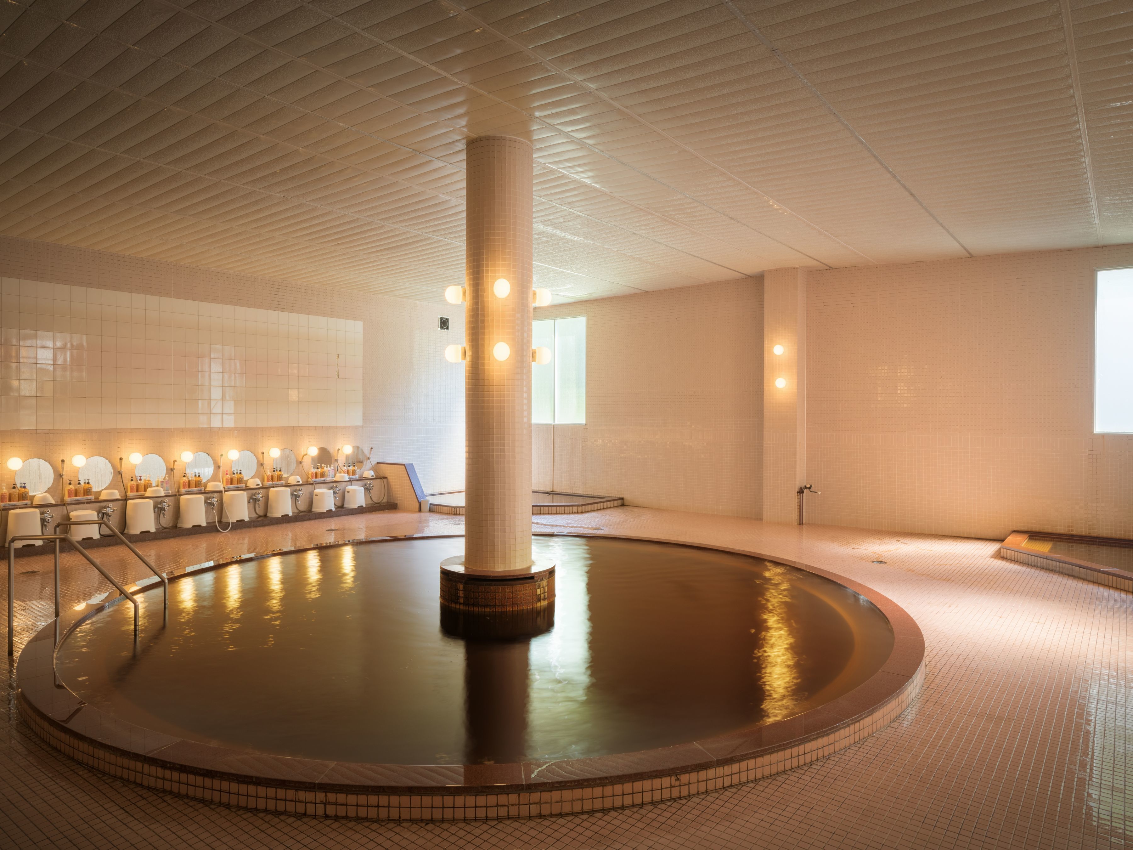 A large indoor pool with a central column, tiled walls, and multiple mirrors along the pool's edge.