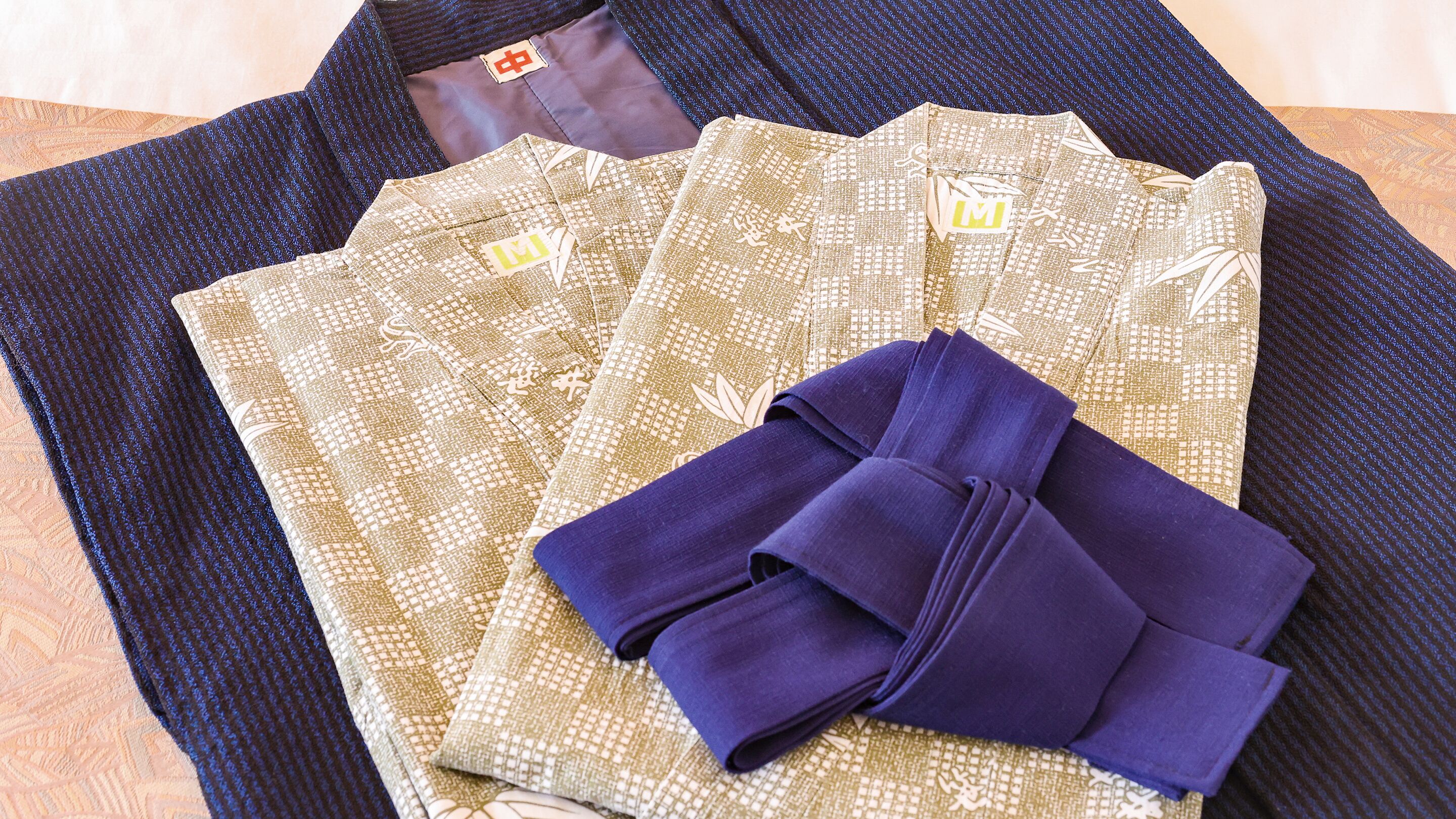 A neatly folded set of traditional Japanese garments, including a kimono and obi, on a patterned fabric.
