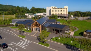 Un hotel moderno con entrada central, varias áreas de estacionamiento y un paisaje verde circundante.