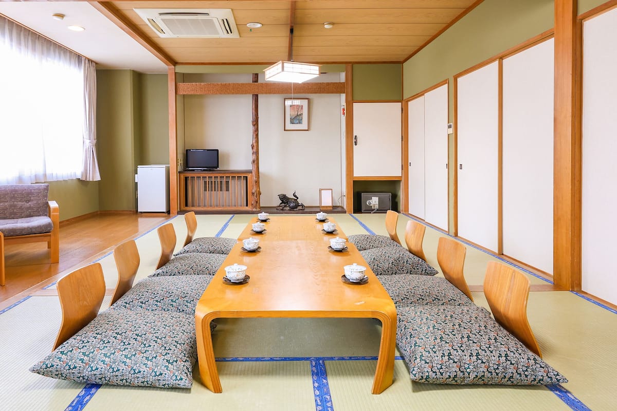 A traditional Japanese-style meeting room with tatami mats, a long wooden table, and cushions.