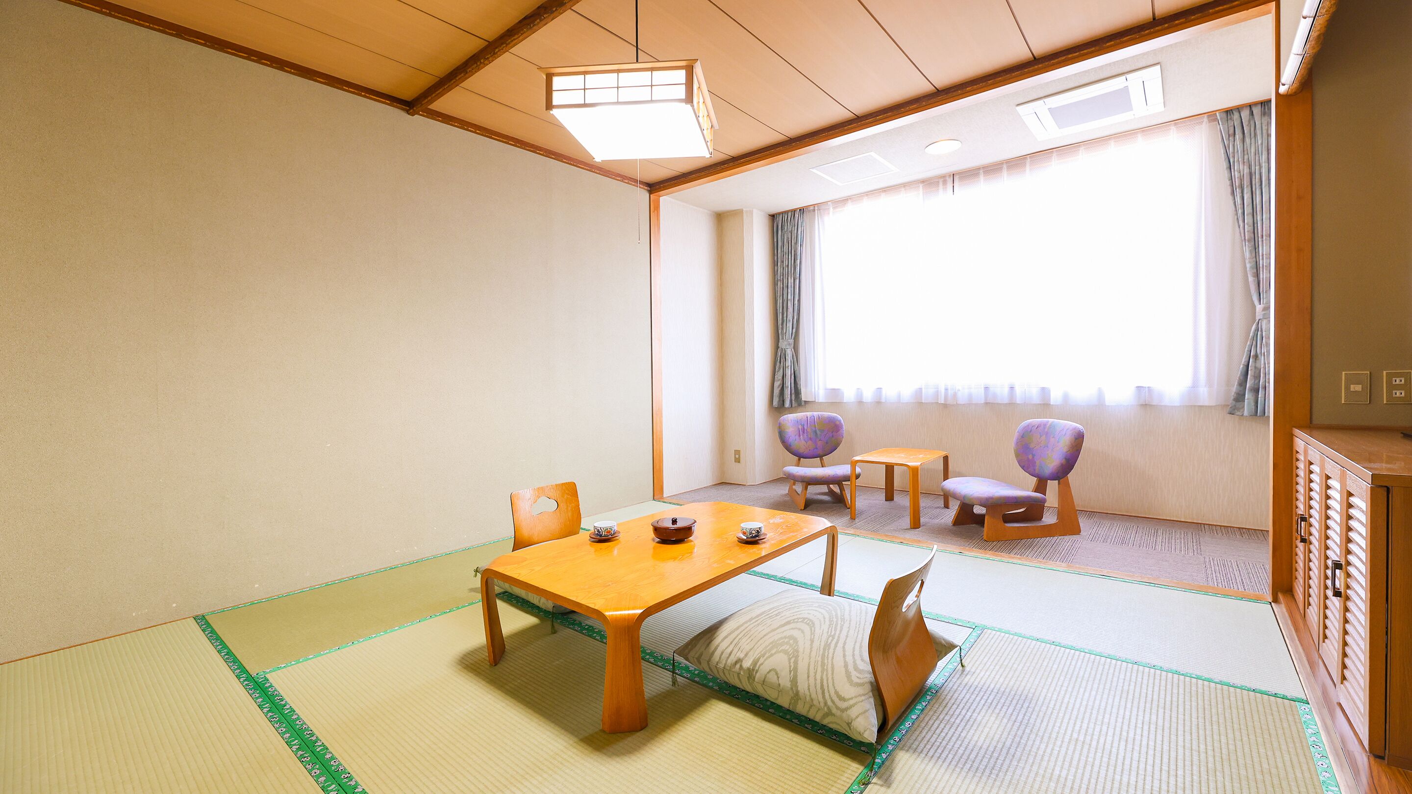 Een traditionele Japanse kamer met tatami vloeren, een lage houten tafel met twee kopjes en een schaal, en twee stoelen.