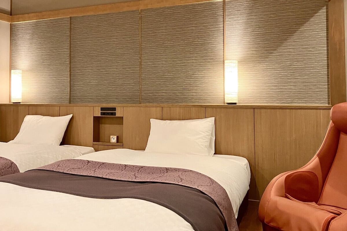 A hotel room with two beds, a wooden headboard, a nightstand, and a red armchair.