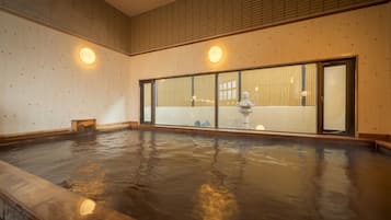 Un onsen japonés tradicional con paredes de madera, una amplia bañera de madera y un farol de piedra.