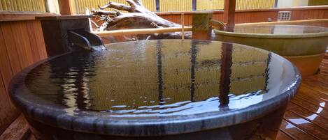 A traditional Japanese onsen with a large stone basin, wooden flooring, and bamboo elements in the background.