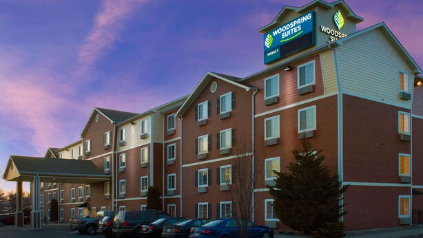 Ett hotell med flera våningar, med en tydlig skylt som visar att det är ett Woodspring Suites-hotell.