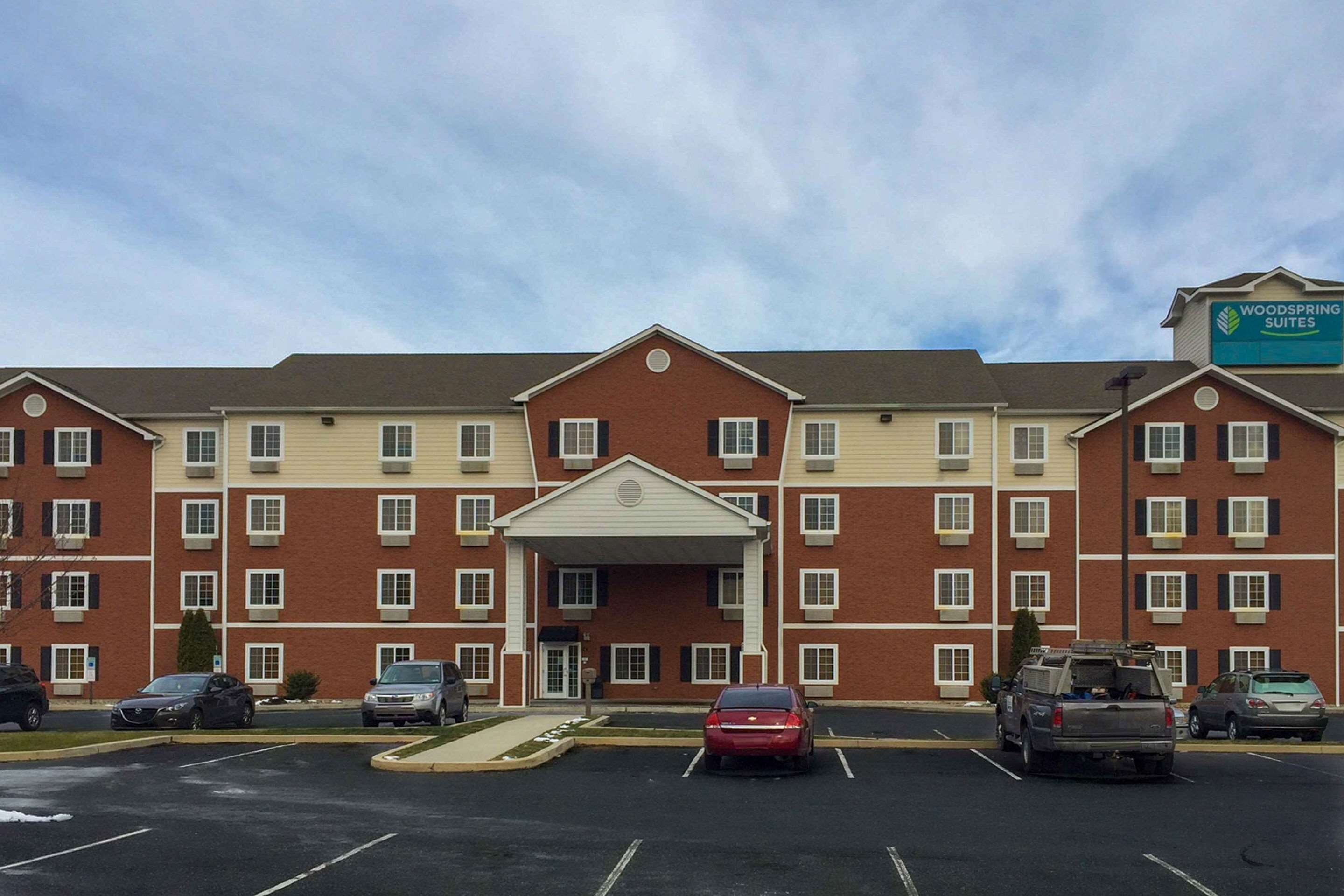 Un hôtel à plusieurs étages, doté d’une entrée principale, d’un parking et d’une enseigne indiquant qu’il s’agit d’un hôtel Woodspring Suites.