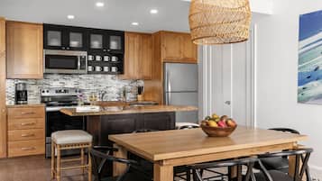 Een moderne keuken met houten kastjes, roestvrijstalen apparatuur en een eethoek met een houten tafel en stoelen.