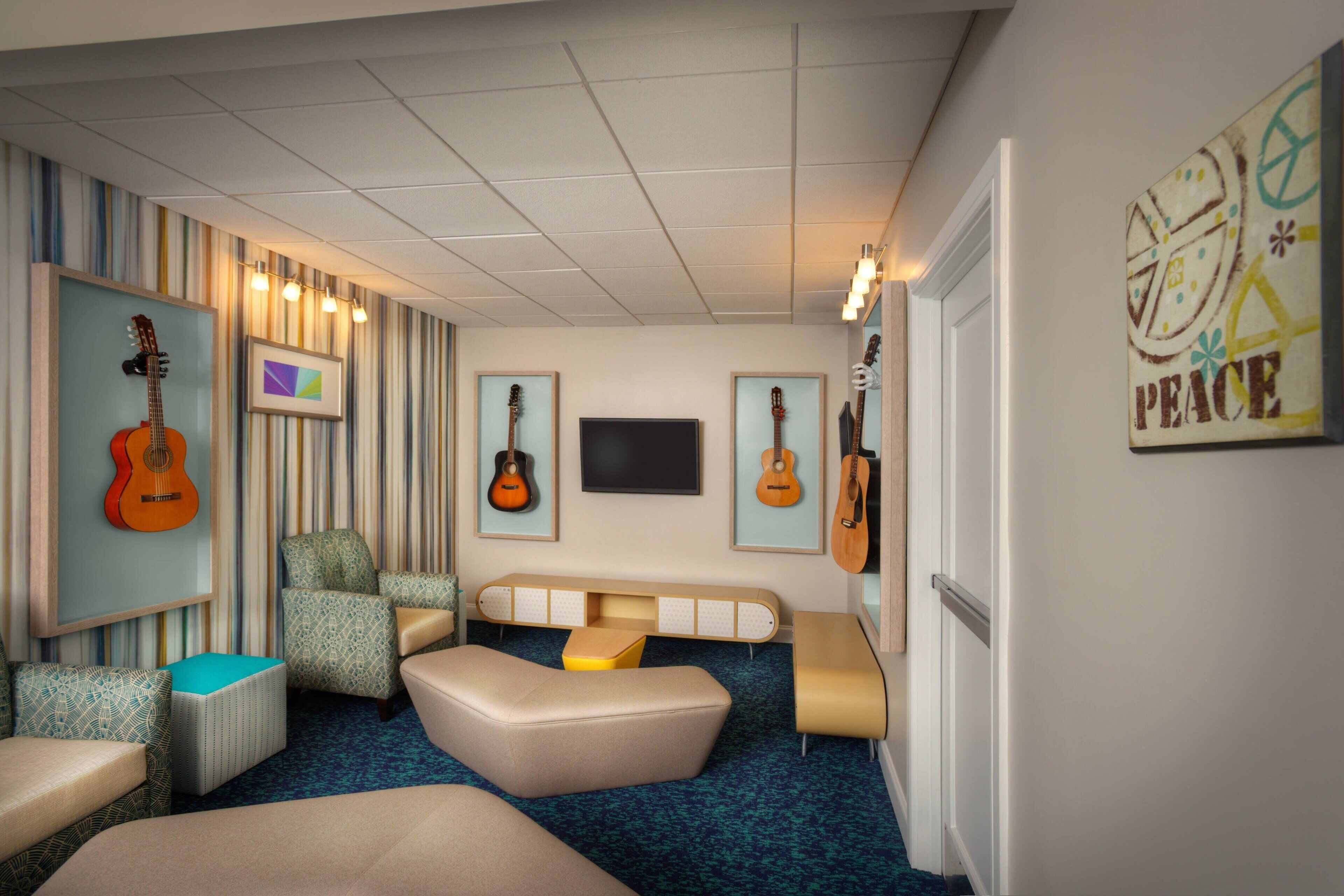 A room with striped wallpaper, a television, and guitars on the wall. There are multiple seating areas, including a sofa and chairs.