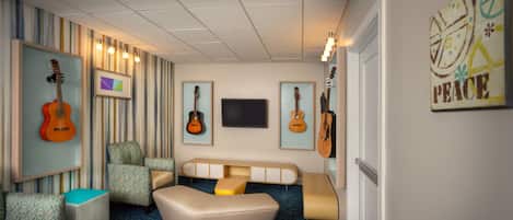 A room with striped wallpaper, a television, and guitars on the wall. There are multiple seating areas, including a sofa and chairs.