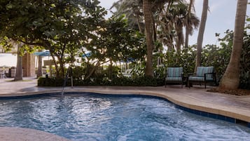 Une piscine à bord incurvé, entourée de palmiers et de chaises longues.