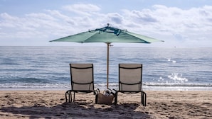 Two beach chairs under a green umbrella facing the ocean.