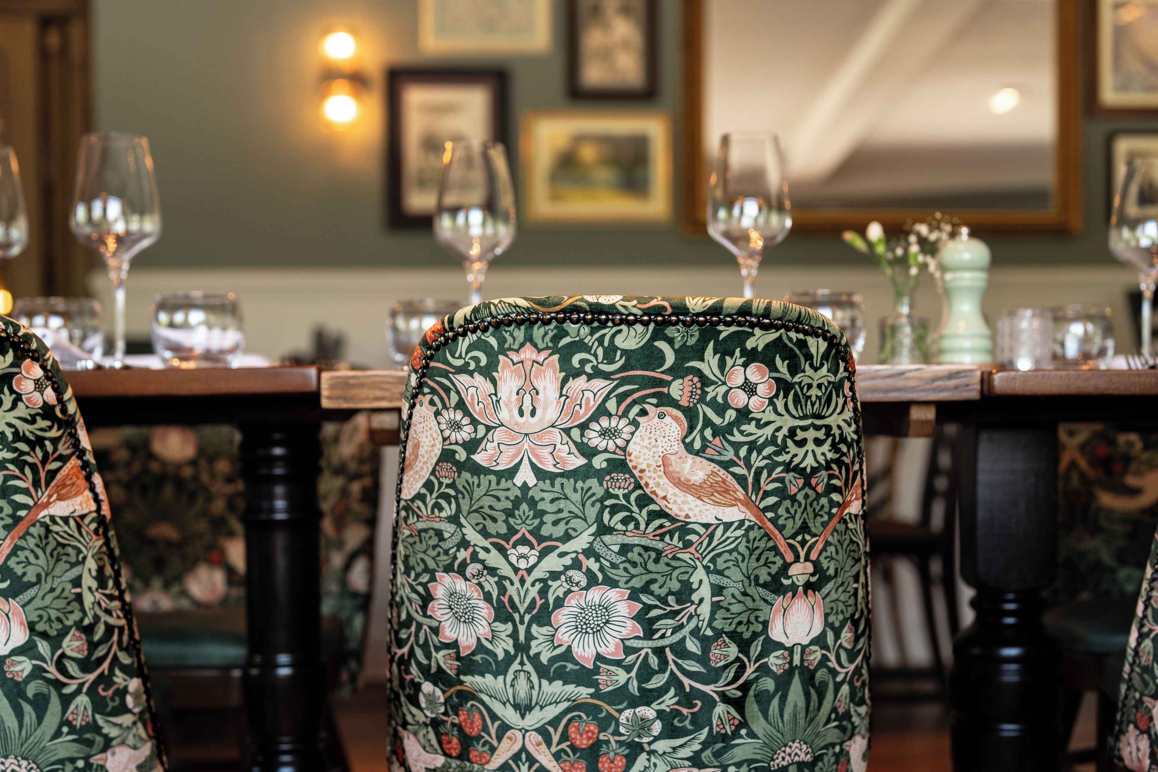 Comedor con sillas ornamentadas y una mesa dispuesta para una comida, enmarcado por obras de arte y cuadros.