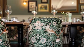 Comedor con sillas ornamentadas y una mesa dispuesta para una comida, enmarcado por obras de arte y cuadros.