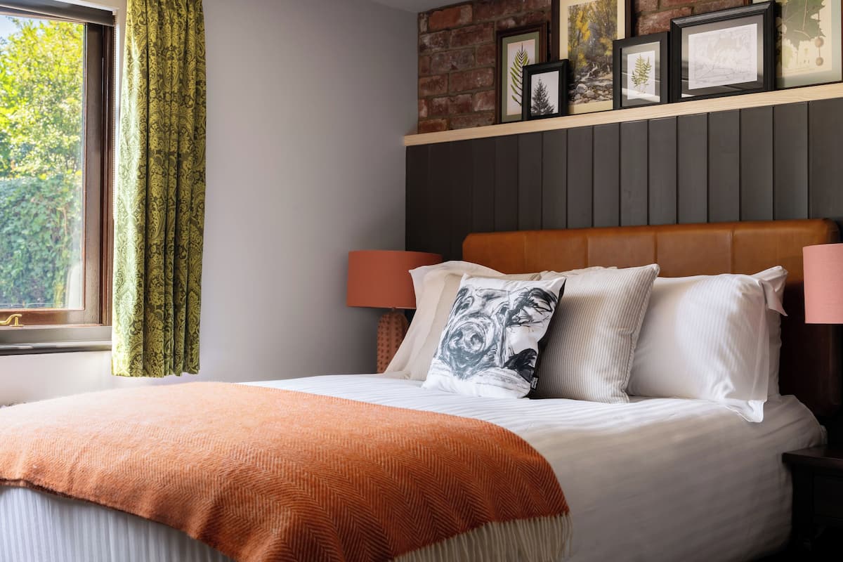 Una camera da letto con un letto, una testiera, una finestra con tende e quadri appesi al muro.