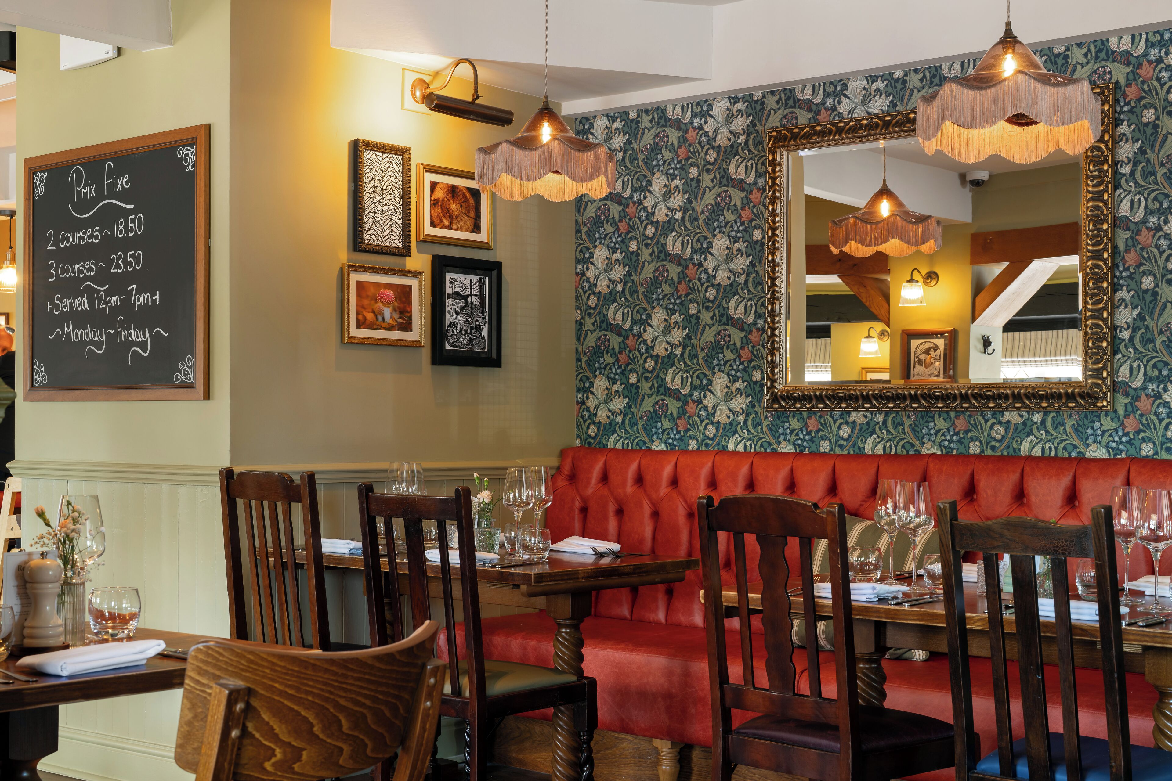 A restaurant interior with a red upholstered booth, wooden tables, and hanging pendant lights.