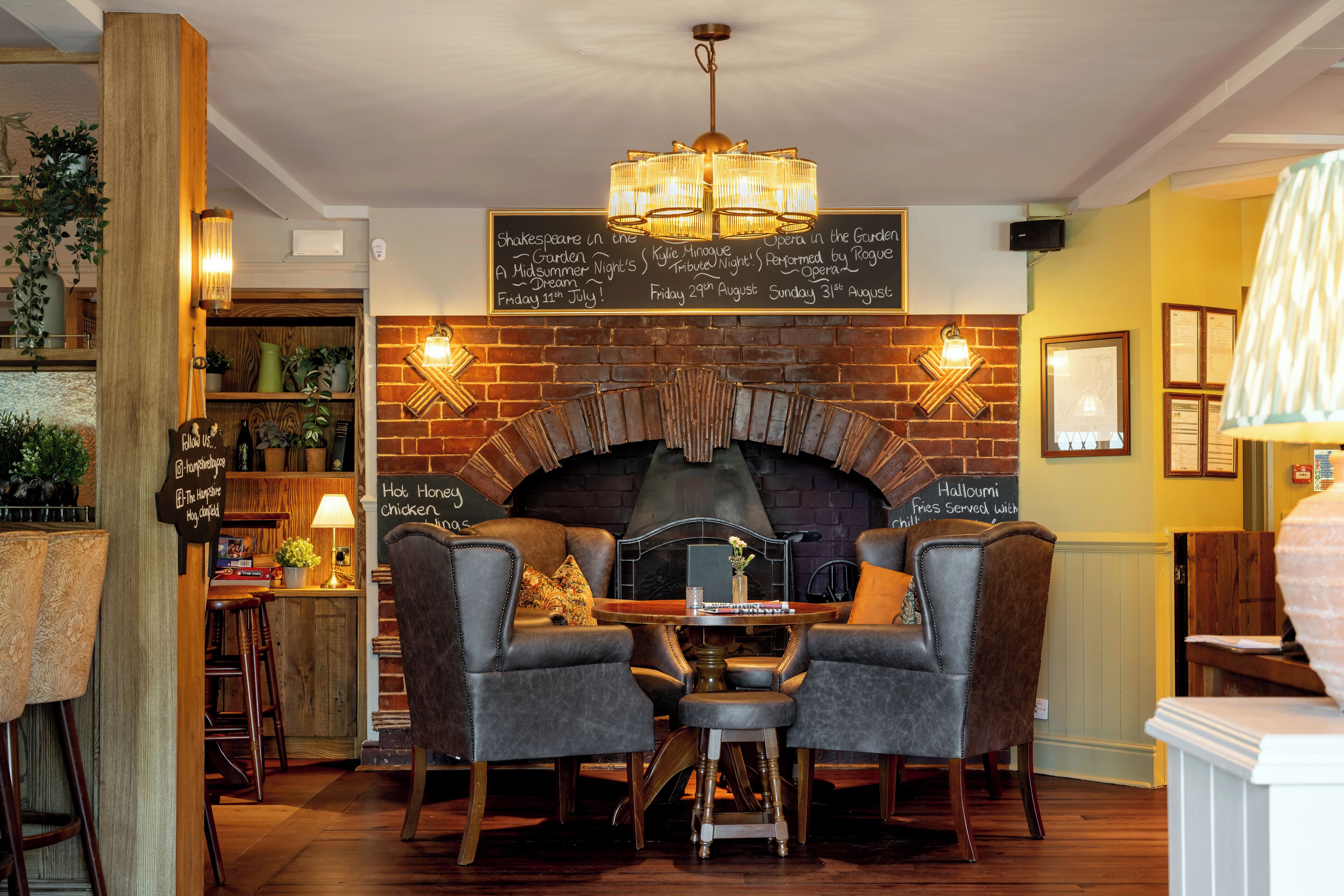 Un pub acogedor con chimenea de ladrillo, dos sillones de cuero y una mesa con lámpara.