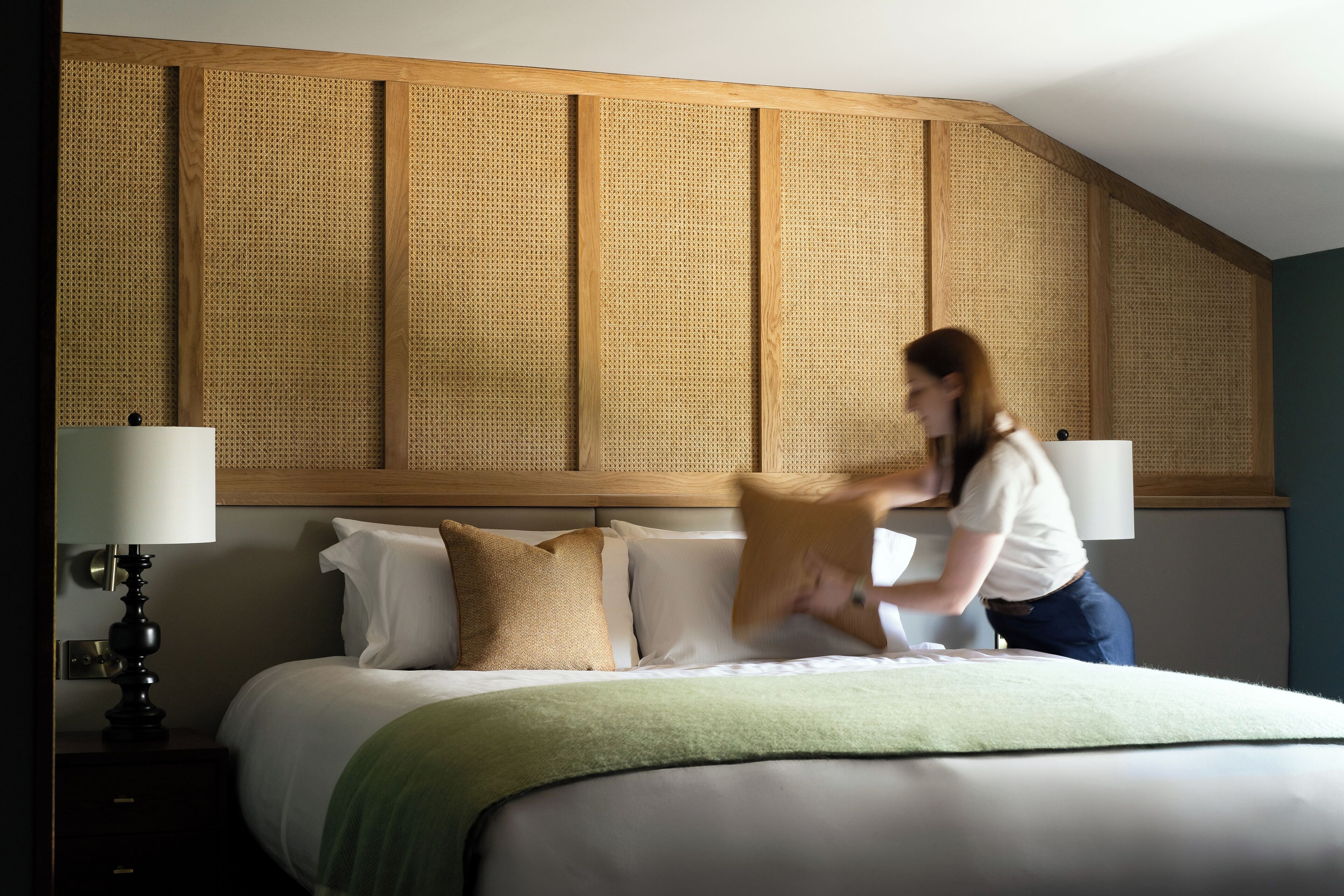 A hotel room with a large bed, a wooden headboard, and a green throw blanket.